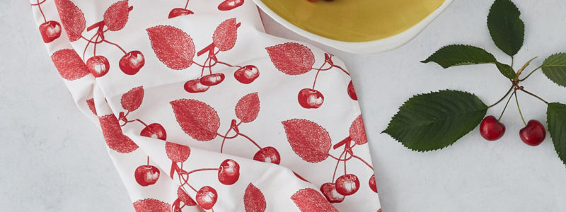 cherry cotton tea towel on a table with a bowl of cherries